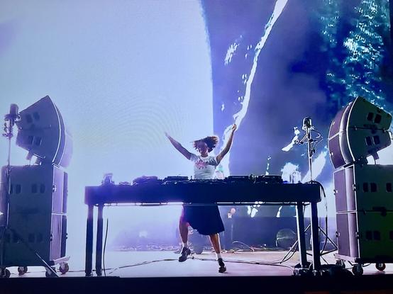 DJ stood behind decks dancing with speakers pointing directly at her.
