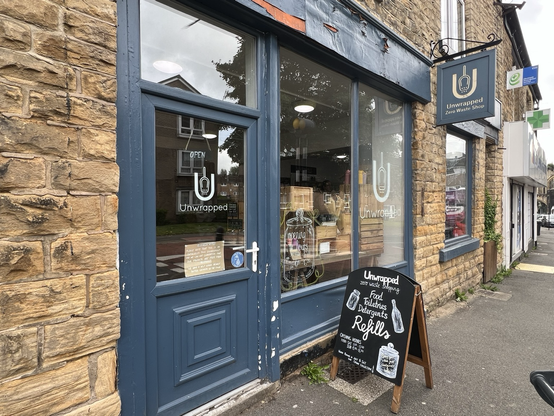 Shop front of the Unwrapped Shop with large windows in blue frames and various items in the display