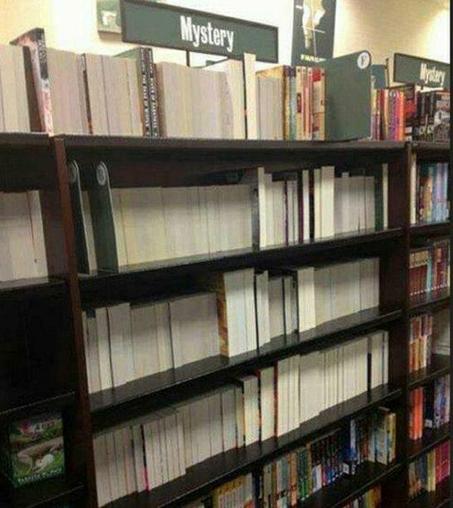 Several rows of books in a bookshop in the Mystery section which is a sign aboved them. All are turned inwards so no spine, titles or author are shown to the buyer