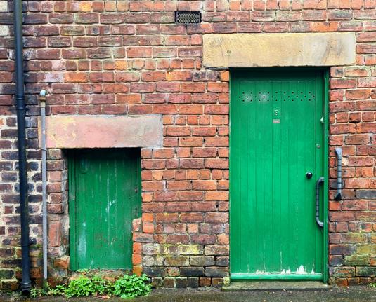 Two greens doors beside eaxhbother on the brick wall of a small building. One os a normal-sized door, the other is a half-sized door.