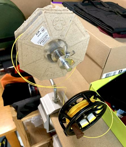 A compostable paper spool with a fly line is on a spooler. A black fly reel is being spooled with the fly line.