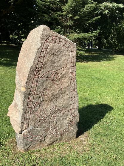 A large stone, with a flat front, engraved with runes. The engraving has been highlighted with red paint to make it more visible. Although this has been done recently, there is evidence that the engravings would have been painted at the time the stones were erected.