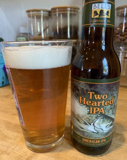 A pint glass with amber-colored IPA and its trout-featured bottle are on a maple wood table.