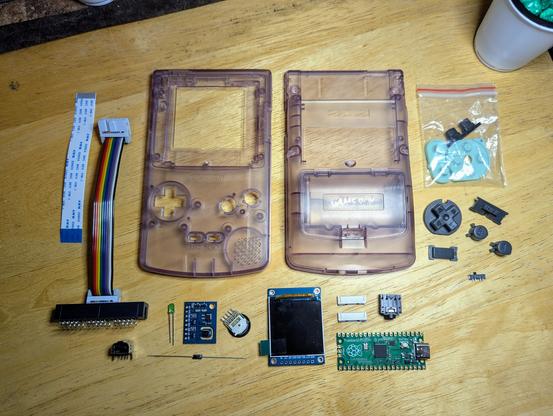 A Game Boy Color case, display, Raspberry Pi Pico, ribbon cables, and various other components.