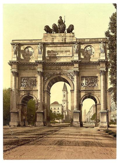 The image depicts a grand stone archway, which is a historic monument known as the Siegestor in Munich, Bavaria, Germany. This architectural structure is notable for its grandeur and intricate design elements. The central part of the arch features statues of people, adding to its prominence and artistic value. There are trees visible in front of the arch, suggesting it's an outdoor setting. The photograph captures the essence of the Siegestor, showcasing its impressive size and craftsmanship that stands as a testament to historical architecture.