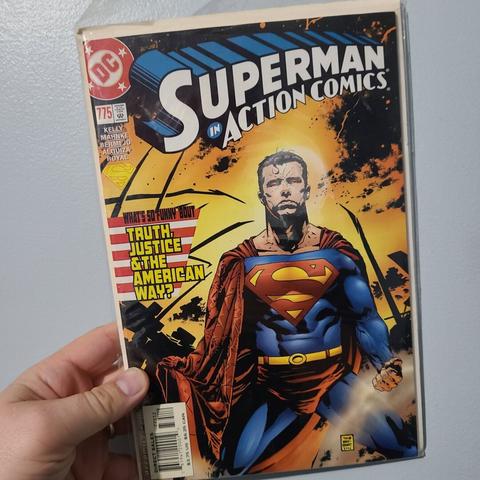 Photograph of a white person's hand holding Superman in Action Comics issue 775 against a light colored wall. The issue appears to have flames in the background as Superman is shown with glowing red eyes, on his knees.