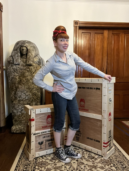 An artist who swears they don’t work in a 1950s diner poses in front of two wooden crates that bear warnings of the fragility of artwork contained within.