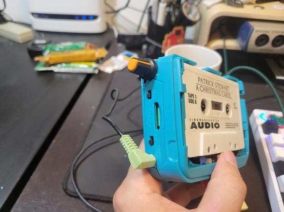 A blue tape walkman without a cover for the cassette, the left side has a rotary knob for attenuation, and a 35mm cable going into the hwadphone jack.
