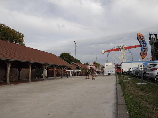 Training spot with the amusement park in the distance.
A parking lot on one side
A roof with people training on the other side
A man on his skateboard on the street in front of us with a younger boy next to him.