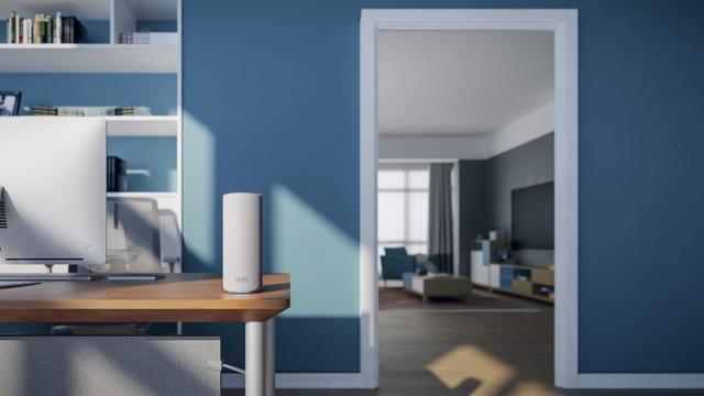 Ein weißer Router in Zylinderform der neuen Netgear Orbi 770-Serie steht in einer Wohnung auf einem Schreibtisch. Foto (c) Netgear.