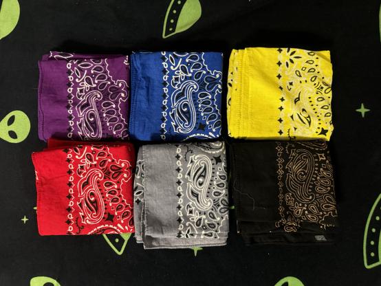 A collection of six folded hankies in various colors: purple, blue, yellow, red, gray, and black, arranged in two rows. The background features a dark textile with alien motifs.