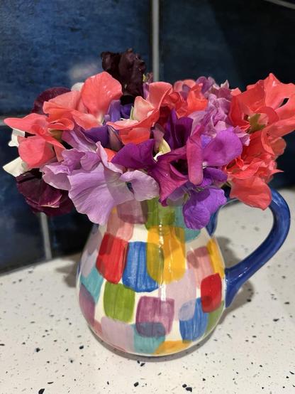 Sweet pea flowers in small white vase with multicoloured brush stroke pattern