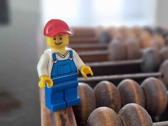 A LEGO figure standing on the edge of the Soviet abacus. The beads on the abacus are between two-thirds and three-quarters the size of the minifig.