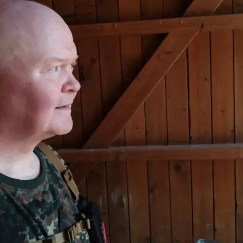 Linksseitig ein Portrait einer Person, im Hintergrund eine braune Holzwand einer Schutzhütte
