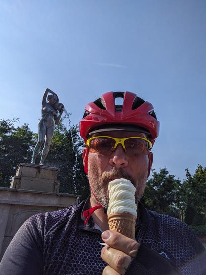 Selfie. W czerwonym kasku i żółtych okularach jem waniliowego loda-świderka, a w tle mam fontannę z nagą kobietą lejącą wodę z dzbana.