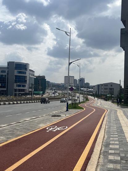 Photo d'une piste cyclable bidirectionnelle avec un enrobé rouge. Elle longe un très large boulevard urbain ayant 3 voies de circulations dans chaque sens et un tramway au milieu.