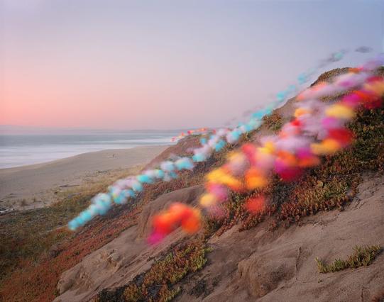 tufts of colorful tulle float down a hill by a beach