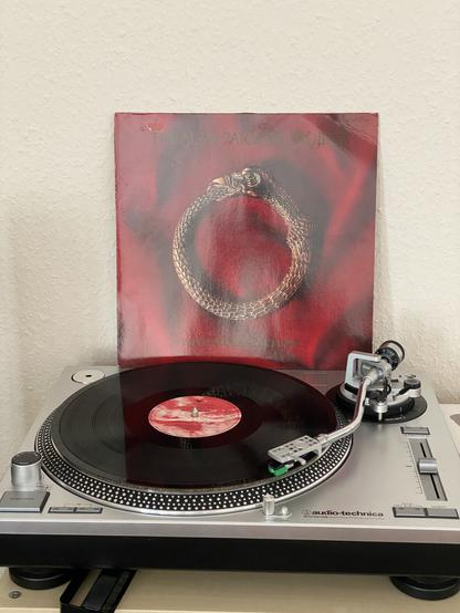 A turntable with the record „vulture culture“ from Alan Parsons Project playing. In the background stands the album cover.