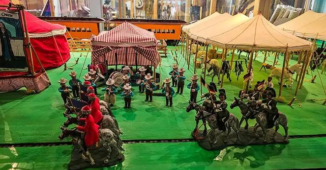 Carved figures of men on horses, a band playing and circus-like tents.