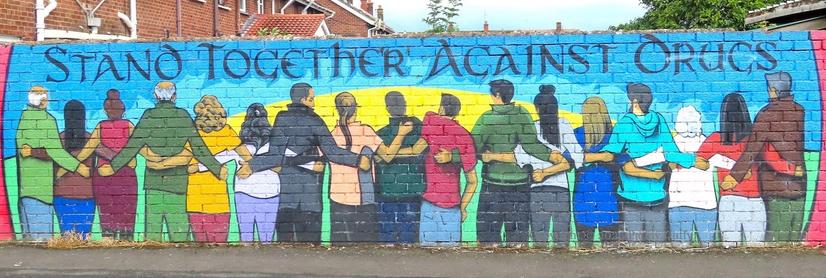 part of a wall-painting with the words "Stand together against drugs" and a line of people arm in arm with their backs to the viewer