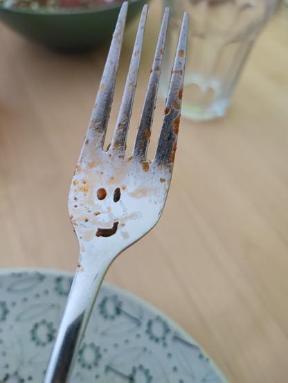 Oberteil einer Gabel. Die Essensreste bilden Augen und Nase. Die Zinken könnten die Haare sein.