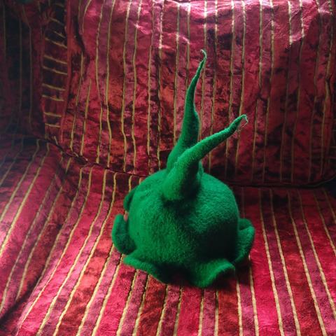 A picture of a green hat with two points and a wavy brim, made of wool. The background is a striped fabric material.