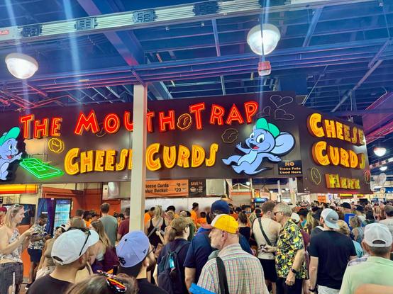 A huge neon sign reads "The Mouth Trap Cheese Curds" with two mice characters, cheese curds in neon, and a neon mouse trap. Below the sign are a ton of people waiting in line