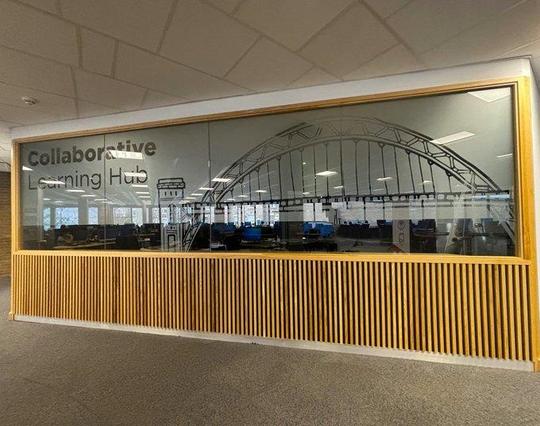 A photograph of the Collaborative Learning Hub at Newcastle University: a wood-framed window featuring an image of the Tyne Bridge.