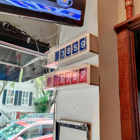 A pair of split-flap or Solari board style displays showing Facebook likes and Instagram follows on the wall of a bar.