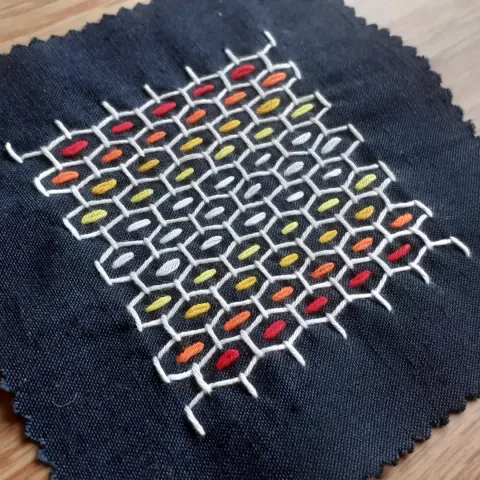 Sashiko sample. White thread hexagin pattern with rainbow strips of stitches insude.