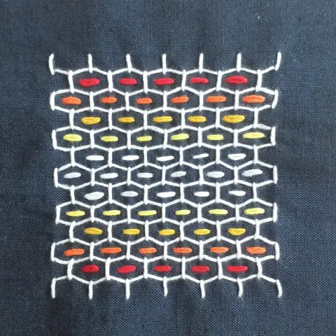 Sashiko sample. White thread hexagin pattern with rainbow strips of stitches insude.