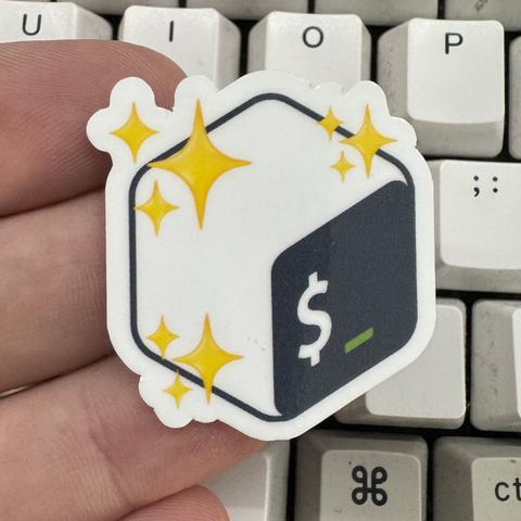A hand holding a sticker featuring a design that includes the Bash logo and decorative sparkles, set against a light-colored keyboard background