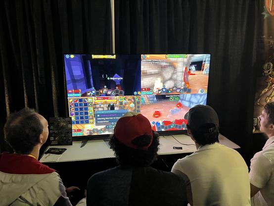 Four gamers sitting in a couch at PAX playing a split screen dungeon crawler visually similar to Minecraft: Barony