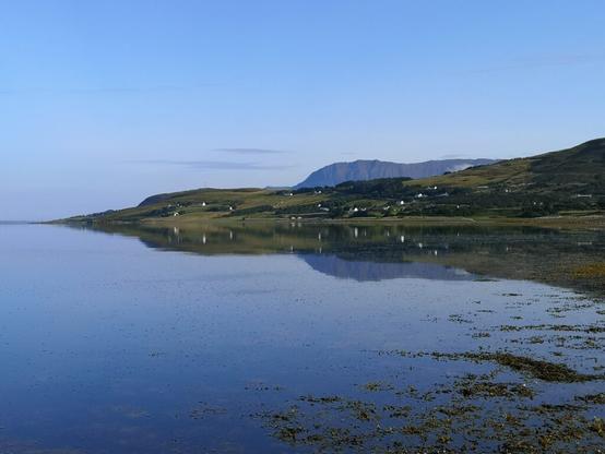 Blick auf das Loch Broom und die Berge im Hintergrund bei Ullapool in Schottland. Vor uns breitet sich eine weite Wasserfläche aus, die links in den Atlantik mündet, Rechts ist das Ufer des Mainlands, das sich mit Berge nach rechts außen erhebt