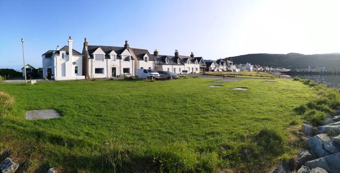Blick auf die Hafenhäuser in Ullapool an der Mole. Wir sehen farbige kleine Häuser, die sich die Straße Richtung Inland entlang ziehen