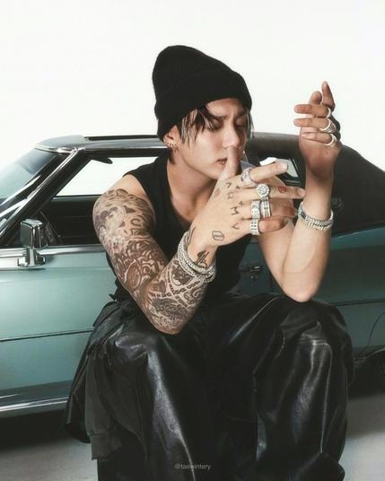 jungkook with big rings big bracelet in black tank and black pants trying to look rnb tough in front of a vintage blue car