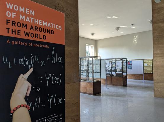 Plakat der Ausstellung "Women of Mathematics from around the world - a gallery of portraits" an einer Säule, im Hintergrund die mathematische Sammlung