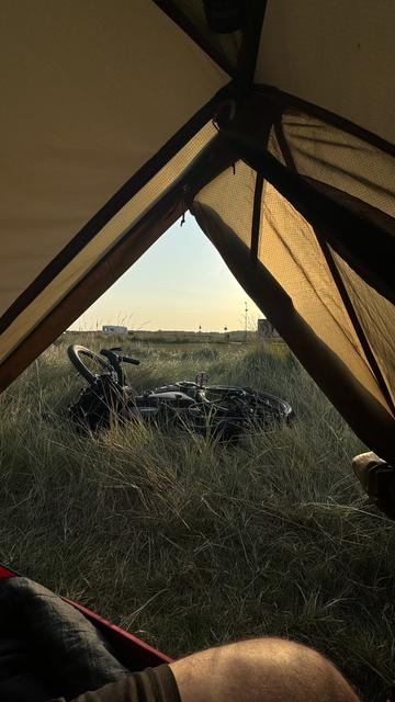 Eine gemütliche Ansicht aus dem Inneren eines Zeltes, das Gras, ein Fahrrad und einen Sonnenaufgang im Hintergrund zeigt.