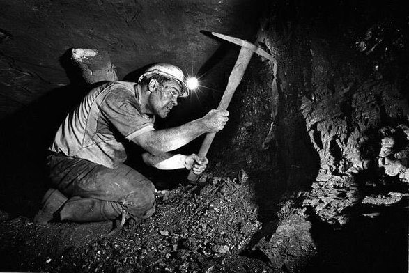 A miner (y’know, an actual grafter) with a pickaxe and lamp working at the coalface.