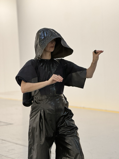 A woman wearing a shiny hooded jumpsuit holds her hands in a specific pose.