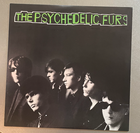 U.S. cover of Psychedelic Furs' debut eponymous album: Black and white shot of five bandmembers, shrouded in shadows with only heads and necks visible, heads turned nearly in profile, eyes closed or with dreamy looks,  on black background.Across the top, "The Psychedelic Furs" in irregularly shaped block letterin bright green.
