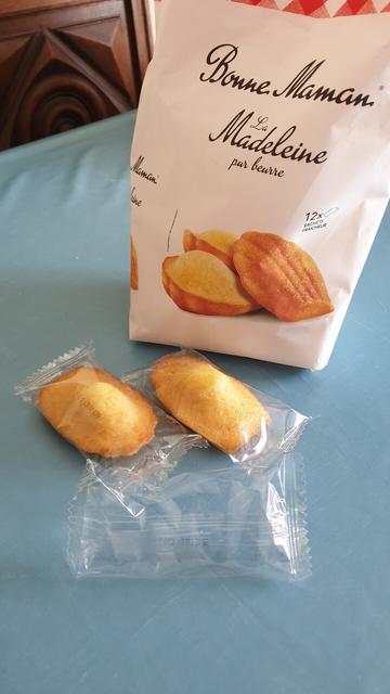 Un paquet de madeleines Bonne Maman sur une toile cirée bleu clair. Devant ce paquet, deux sachets avec une madeleine dedans et un sachet contenant seulement de l'air.