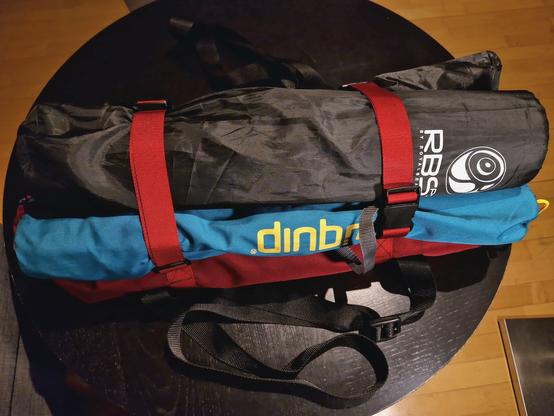 Mehrere Campinghocker, mit Spanngurten auf der Tasche befestigt.