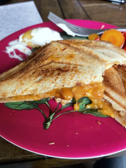 A curry bean jaffle dripping beans and cheese on a brightly colored plate.