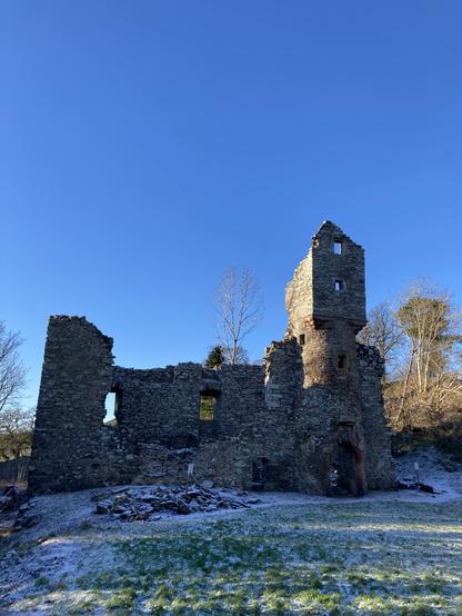 The remains of Torwoodleee Tower, a rectangular block with a round tower rising up at one end. Cold blue skies behind and a scraping of snow on the ground.