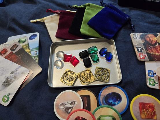 A photo of the components of the Splendour board game, supplemented with more realistic gems and coins from Etsy to replace the included tokens.