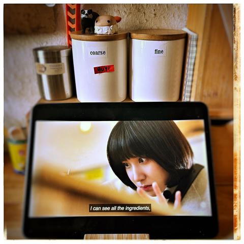 A kitchen counter scene with two labeled jars marked "coarse" and "fine." Above them, small figurines, a badger and an ebi nigiri (shrimp sushi), are displayed. A tablet shows a close-up of a person with a short hairstyle, engaged in a culinary moment, with subtitles stating «I can see all the ingredients.».