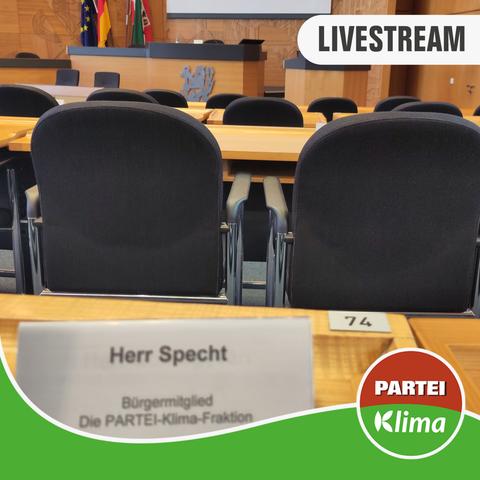 Zu sehen ist der Plenarsaal des Düsseldorfer Rathauses aus der Perspektive unseres Fraktionista Nick im Ausschuss für Gesundheit & Soziales. In der rechten oben Ecke klebt unser LIVESTREAM Label, im unteren Bereich findet sich unsere grüne Wandelwelle, nebst dem Die PARTEI-Klima-Fraktionslogo auf der rechten Seite.