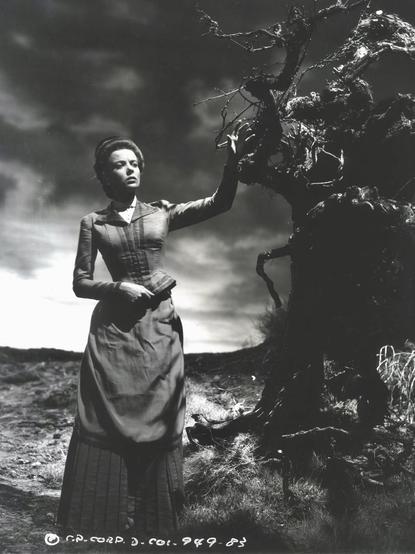 Lupino in Victorian dress in a gloomy outdoor scene, dramatic lighting. She reached up towards a scraggly, dead-looking tree.