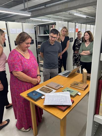 Kultusministerin Schopper und weitere Personen stehen an einem Tisch, auf dem Bücher liegen. Im Hintergrund sind Archivschränke. Foto: Kultusministerium Baden-Württemberg